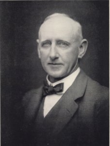 Image of a white man with a thin head of hair, wearing a blazer with a white shirt and a bow tie.
